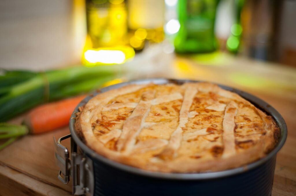 A freshly baked quiche on a wooden table with fresh vegetables nearby.